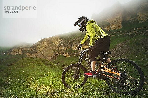 Ein Mann mit Berghelm und Mountainbike fährt bei bewölktem Wetter durch die schöne Natur bergab