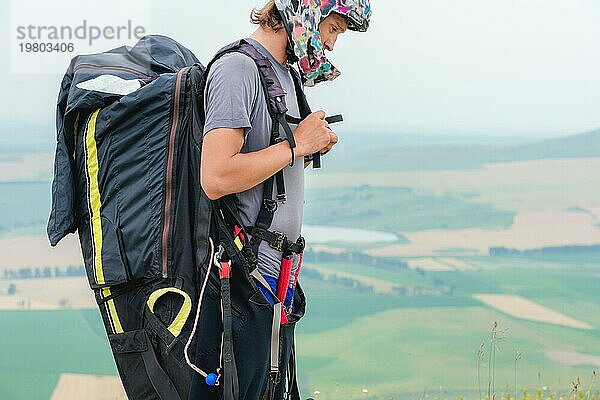 Nahaufnahme eines professionellen Gleitschirmfliegers mit einem Kokon auf seinen Schultern Knöpfe Helm schaut zur Seite. Paraglider Sport Konzept