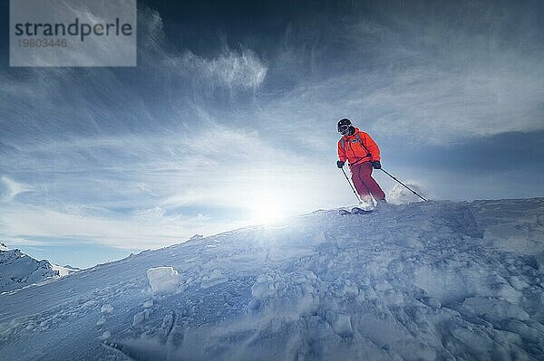 Ein männlicher Skisportler springt an einem sonnigen Tag von einem schneebedeckten Hang vor dem Hintergrund einer Berglandschaft mit schneebedeckten Bergen. Das Konzept des Wintersports