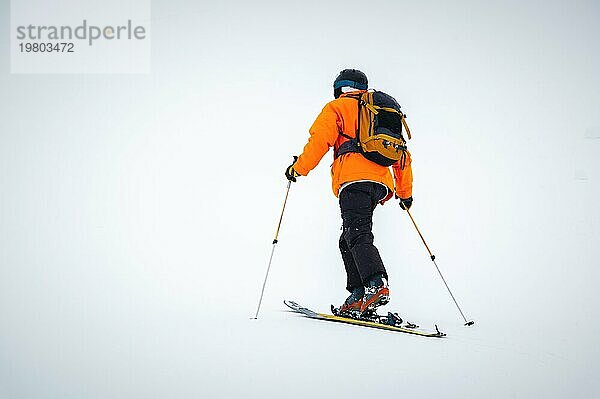 Winterskitour bei bewölktem Wetter  schneebedeckte Berge vor der Kulisse eines Gletschers. Skifahrer Mann in voller Ausrüstung klettert bergauf in einer Skitour