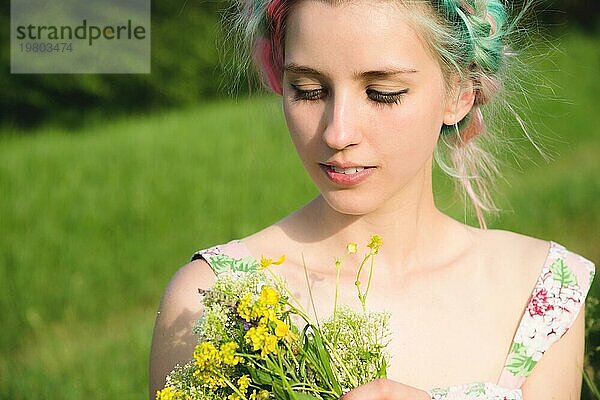 Porträt eines jungen  glücklich lächelnden Mädchens in einem Baumwollkleid mit einem Strauß Wildblumen