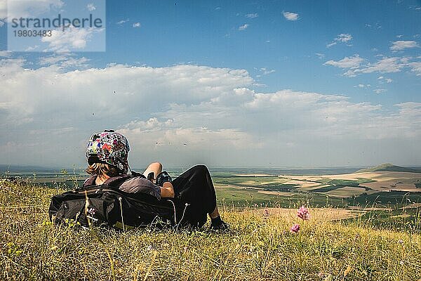 Ein professioneller Gleitschirmflieger in voller Ausrüstung und mit Helm liegt auf dem Gras hoch in den Bergen und schaut in die Wolken