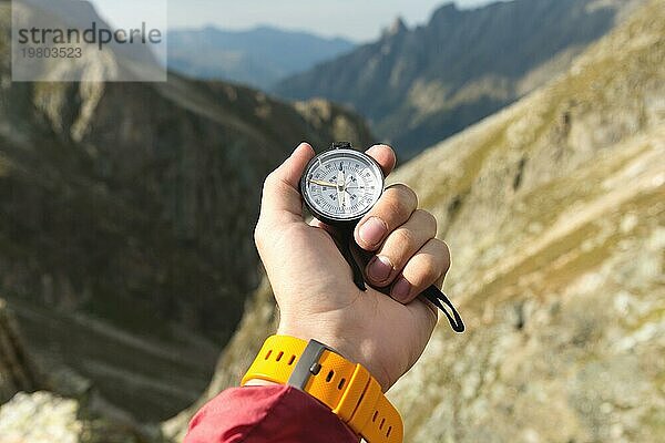 Ein Mann hält einen Taschenmagnetkompass zur Navigation vor dem Hintergrund eines felsigen Abhangs und eines Berges in der Hand. Das Konzept  einen Weg zu finden. Freiheit gewinnen. Freiheit der Wahl