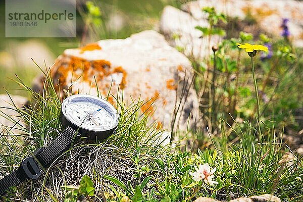 Ein Magnetkompass liegt auf einem Stein neben dem Gras