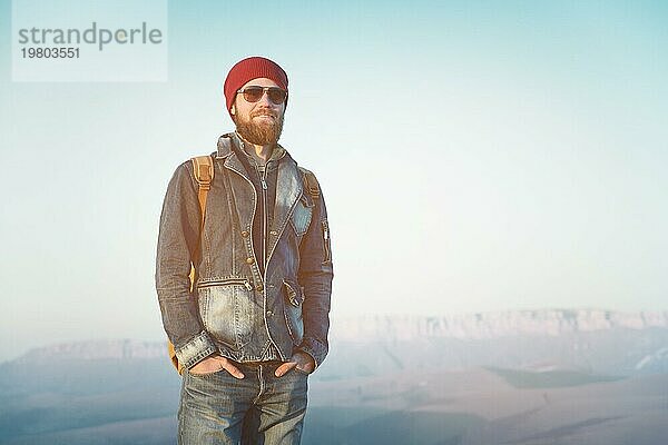 Hipster junger Mann mit Bart und Schnurrbart und Sonnenbrille posiert vor dem Hintergrund der Berge