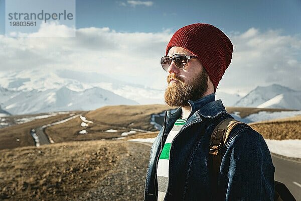 Hipster junger Mann mit Bart und Schnurrbart und Sonnenbrille posiert vor dem Hintergrund der Berge