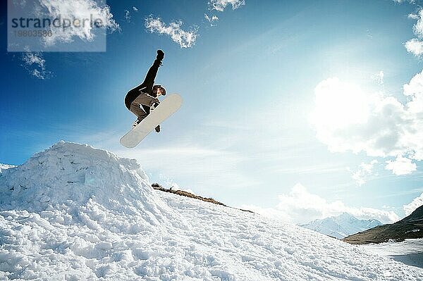 Stylish junges Mädchen Snowboarder macht den Trick beim Springen von einem Schnee Kicker gegen den blaün Himmel Wolken und Berge im Frühjahr. Das Konzept der Frühling Snowboarden in den Bergen und die Schließung der Winter Ski Saison