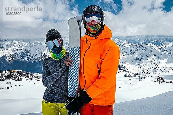 Junges Paar von Skifahrern Mann und Frau unerkennbar in Snowboarding Ausrüstung Masken auf dem Hintergrund. von schneebedeckten Bergen hoch in einem Skigebiet an einem sonnigen Tag