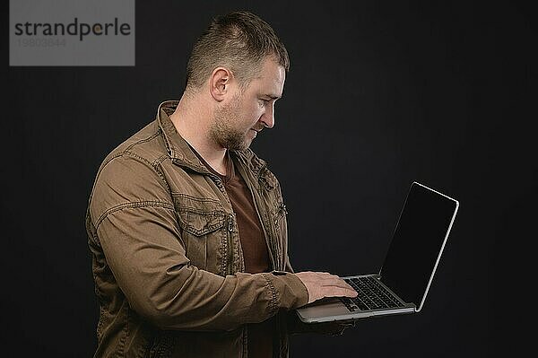 Kaukasischer Mann mittleren Alters benutzt einen Laptop  während er im Studio steht. Porträt eines Freiberuflers beim Surfen im Internet