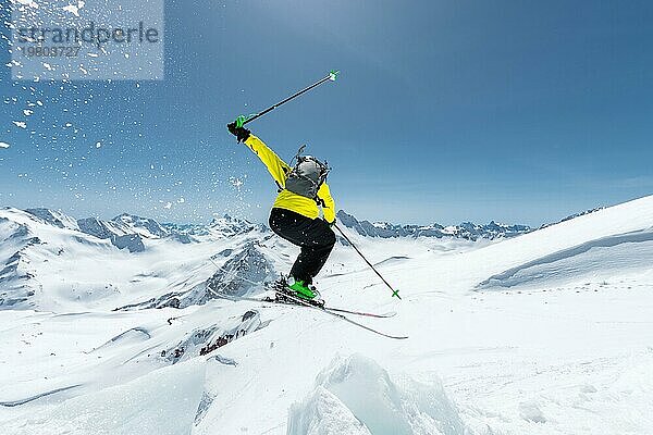 Ein Skifahrer in voller Sportausrüstung springt von der Spitze des Gletschers in den Abgrund  vor dem Hintergrund des blaün Himmels und der schneebedeckten Berge des Kaukasus. Blick von hinten. Elbrus Gebiet. Russland