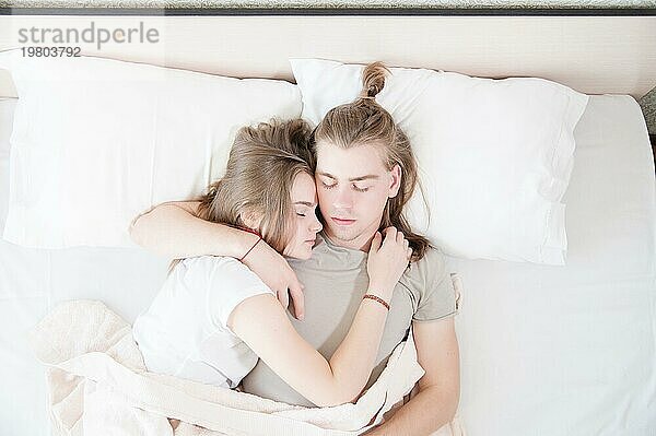 Ein junges Paar moderner Männer und Frauen schläft in ihrem weißen Bett in einer Umarmung. Das Konzept einer jungen modernen Familie und Schlafprobleme