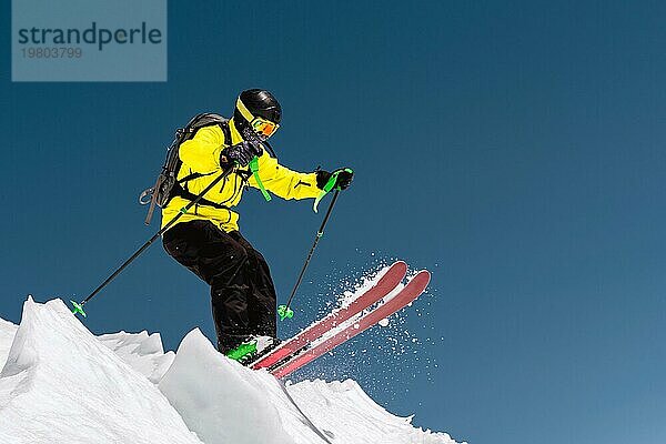 Ein Skifahrer in voller Sportausrüstung springt von der Spitze des Gletschers in den Abgrund vor dem Hintergrund des blaün Himmels und der schneebedeckten Berge des Kaukasus. Elbrus Gebiet. Russland