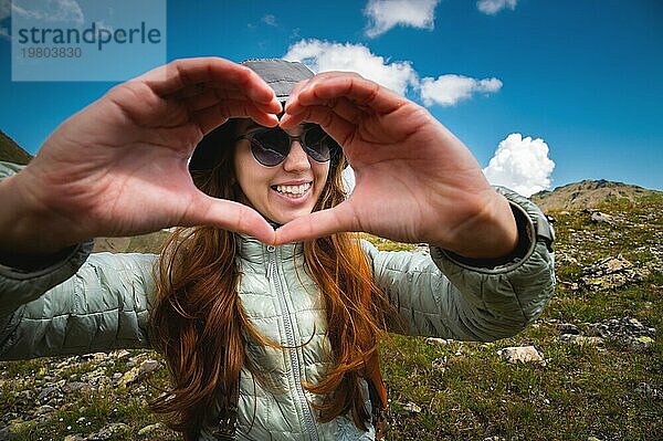 Hände in Form eines Liebesherzens. Eine junge Frau macht ein Herz mit ihren Händen. Mädchen Tourist auf der Spitze des Berges mit einem Rucksack  das Konzept der Liebe für die Natur