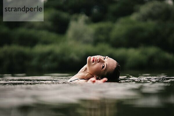 Ein junges  schlankes  schönes und heißes Mädchen mit nassen Haaren und großen Lippen schwimmt im See  reist zu Wasserfällen  entspannt sich am See