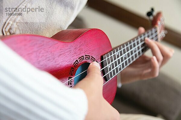 Weibliche sanfte Hände  in denen eine rote Holz Ukulele liegt  Nahaufnahme. Hipster Mädchen Hobby  zu Hause