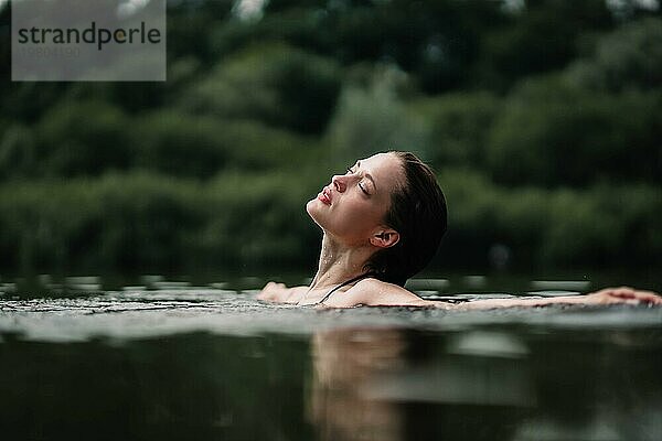 Ein junges  schlankes  schönes und heißes Mädchen mit nassen Haaren und großen Lippen schwimmt im See  reist zu Wasserfällen  entspannt sich am See