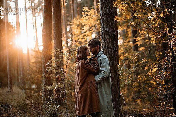 Schöne modische Paar in der Liebe im Wald bei Sonnenuntergang im Herbst  romantische Datum in Regenmäntel  trendy Mann und Frau