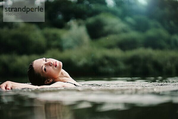 Ein junges  schlankes  schönes und heißes Mädchen mit nassen Haaren und großen Lippen schwimmt im See  reist zu Wasserfällen  entspannt sich am See