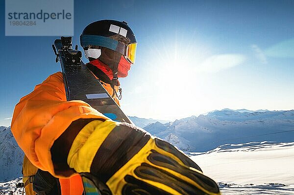 Skifahrer in den winterlichen Bergen vor dem Hintergrund eines sonnigen Himmels  Weitwinkel von unten  ein Mann hält die Skier auf seiner Schulter