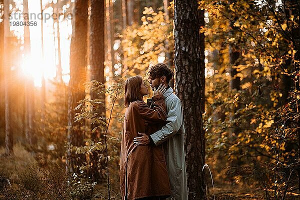 Schöne modische Paar in der Liebe im Wald bei Sonnenuntergang im Herbst  romantische Datum in Regenmäntel  trendy Mann und Frau