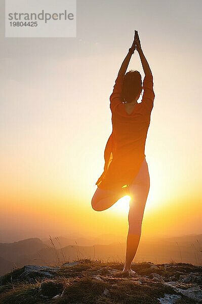 Eine Frau steht in einer Yogapose gegen die Sonne in den Bergen  eine Silhouette einer sportlichen Frau