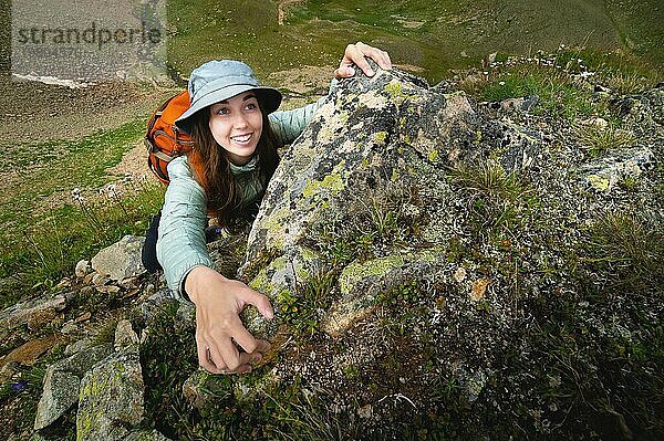 Glückliche Frau klettert beim Trekking im Freien auf einen Felsen. Unbekümmerter Rucksacktourist lächelt in die Kamera