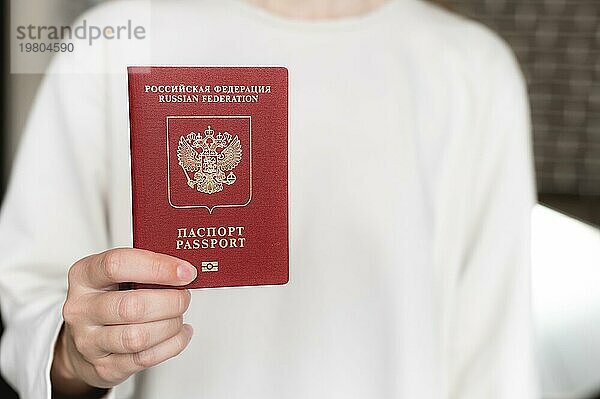 Ausländischer Reisepass der Russischen Föderation. Menschliche weibliche Hand mit einem russischen Pass Nahaufnahme auf dem Hintergrund eines weißen Pullovers  selektiver Fokus  Unschärfe