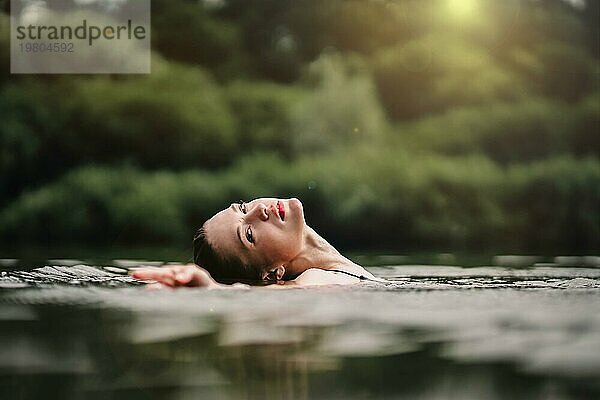 Ein junges  schlankes  schönes und heißes Mädchen mit nassen Haaren und großen Lippen schwimmt im See  reist zu Wasserfällen  entspannt sich am See