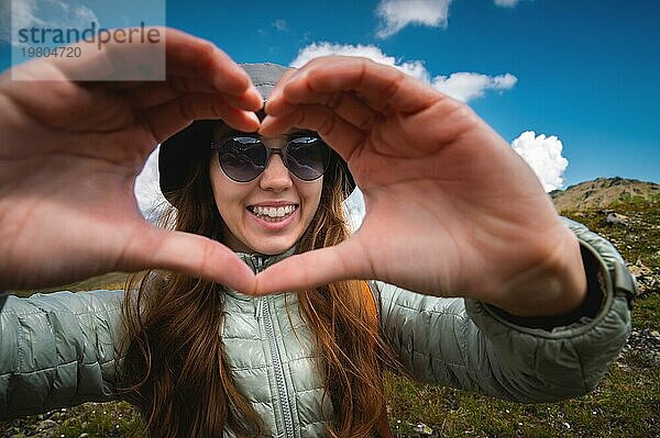 Lächelnde junge Frau zeigt Finger Geste Zeichen des Herzens  Liebe in den Bergen  glücklich Tourist