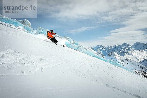 Off Piste Skifahrer auf einem Gletscher hinunter eine schöne alpine Landschaft. Blaür  bewölkter Himmel im Hintergrund und hohe Berge. Freier Raum für Text