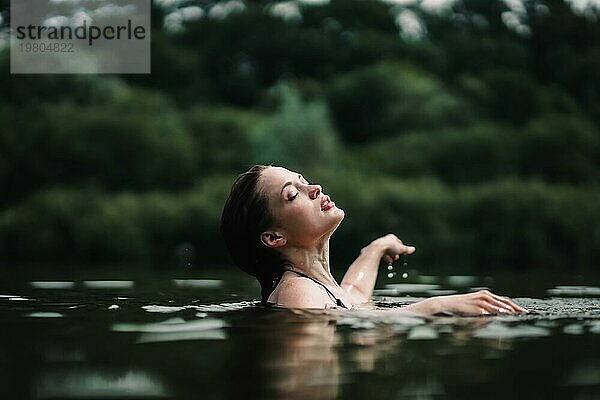 Ein junges  schlankes  schönes und heißes Mädchen mit nassen Haaren und großen Lippen schwimmt im See  reist zu Wasserfällen  entspannt sich am See