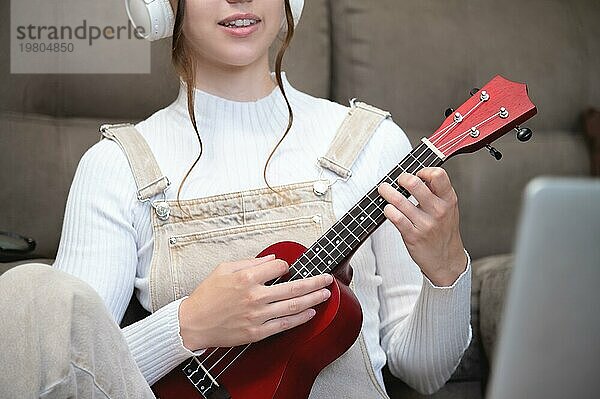 Nahaufnahme  eine Frau oder ein Mädchen spielt Ukulele  während sie zu Hause auf dem Boden sitzt. Fernunterricht