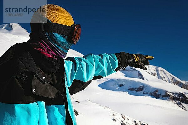 Rückseite Porträt eines Skifahrers in den Spitzen der Berge ohne Skimaske mit einem Schal im Gesicht  der seine Augen verengt und in die Kamera vor dem Hintergrund der schneebedeckten Berge schaut