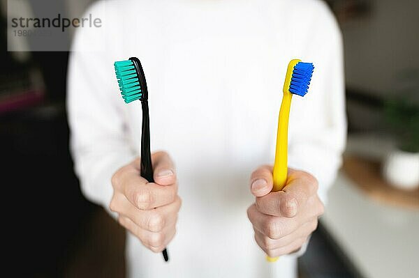 Die Hand einer Frau hält zwei Zahnbürsten. Zahnärztliche Richtung  das Thema der morgendlichen Hygiene eines Ehepaares