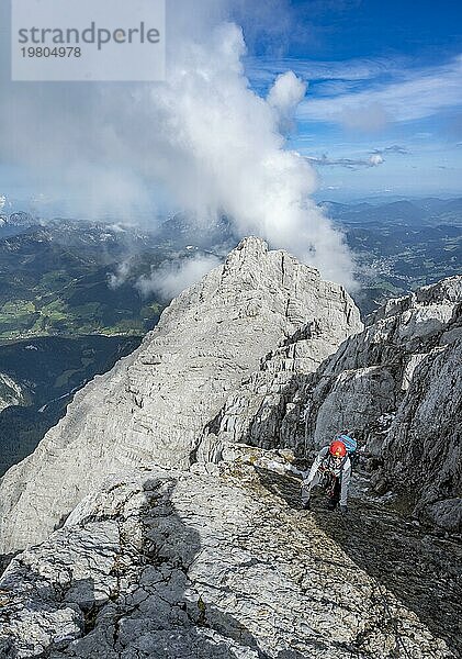 Bergsteigerin in einem mit Stahlseil gesicherten Klettersteig  steile felsige Bergflanke  Watzmann Überschreitung zur Watzmann Mittelspitze  Ausblick auf Bergpanorama mit Watzmann Hocheck Gipfel  Nationalpark Berchtesgaden  Berchtesgadener Alpen  Bayern  Deutschland  Europa