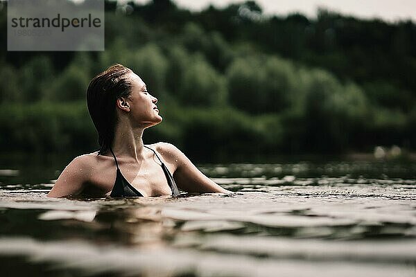 Junges schlankes schönes und heißes Mädchen mit nassen Haaren schwimmt im See  Reisen  Entspannung am See
