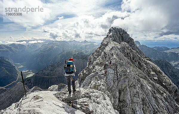 Bergsteigerin in einem mit Stahlseil gesicherten Klettersteig  schmaler felsiger Berggrat  Watzmann Überschreitung zur Watzmann Mittelspitze  Ausblick auf Bergpanorama mit Steinernes Meer  Nationalpark Berchtesgaden  Berchtesgadener Alpen  Bayern  Deutschland  Europa