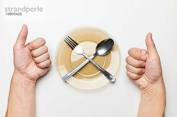 Männerhände zeigen eine Klasse Geste  ein weißer Tisch  ein leerer Teller und eine Gabel und ein Löffel liegen darauf  Draufsicht. leckeres Essen Idee