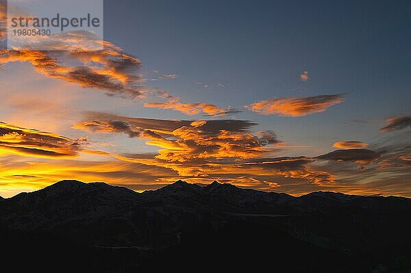 Dunkelorangefarbene Landschaft  Bergsilhouette mit Blick auf die hinter den Wolken leuchtenden Sonnenstrahlen bei Sonnenuntergang