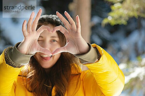 Ein universelles Zeichen der Liebe und Romantik in Form eines Herzens  hergestellt von den Händen eines fröhlichen Mädchens in einem Winterwald