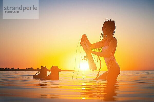 Sexy Sport Mädchen Surfer Wakeboarder mit Brett bei Sonnenuntergang Strand  heiße Silhouette im Meer stehen