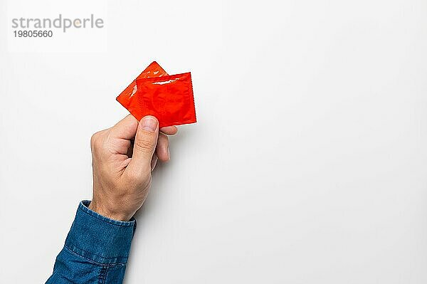 Die Hand eines Mannes hält ein rotes Kondom auf weißem Hintergrund. Ansicht von oben. Das Konzept der Bewahrung der Sexualität