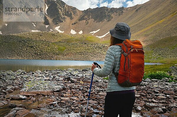 Rückenansicht von stilvollen Hipster Frau mit Rucksack  grauen Hut Blick auf Bergsee während Outdoor Erholung. Entspannen Sie sich beim Entspannen auf einem Konzept Reise