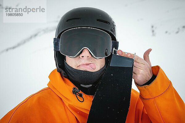 Ein junger Skifahrer steht im Winter auf einem Berghang und zeigt seine Zunge