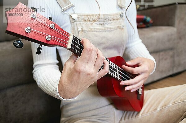 Nahaufnahme  Ukulele in weiblichen Händen  Hipster lernt zu Hause ein Musikinstrument zu spielen  sitzt auf dem Boden neben dem Sofa