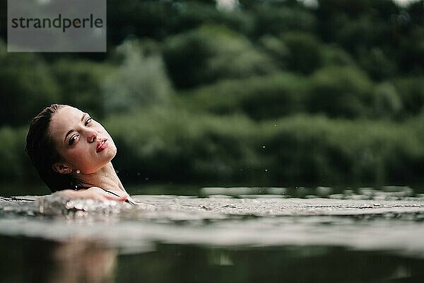 Ein junges  schlankes  schönes und heißes Mädchen mit nassen Haaren und großen Lippen schwimmt im See  reist zu Wasserfällen  entspannt sich am See