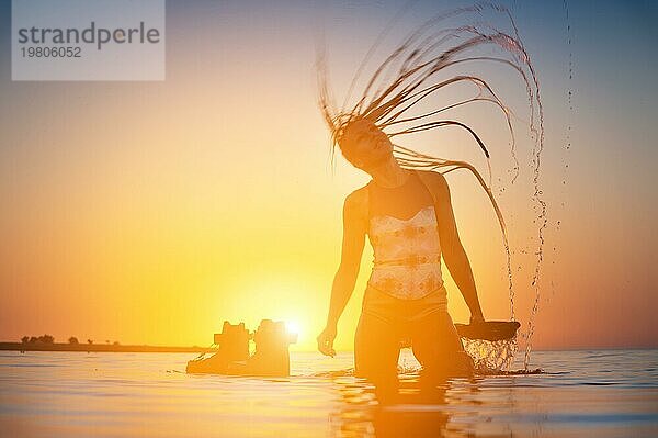 Silhouette einer schlanken jungen Athletin Kitesurfer schwimmt bei Sonnenuntergang im Meer neben ihrem Kite Board