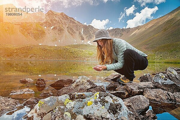 Ein junges Mädchen füllt ihre Hände mit Wasser aus einem Bach eines kalten Bergsees  um zu trinken und sich zu erfrischen. Glücklicher Wanderer auf einer Wanderung