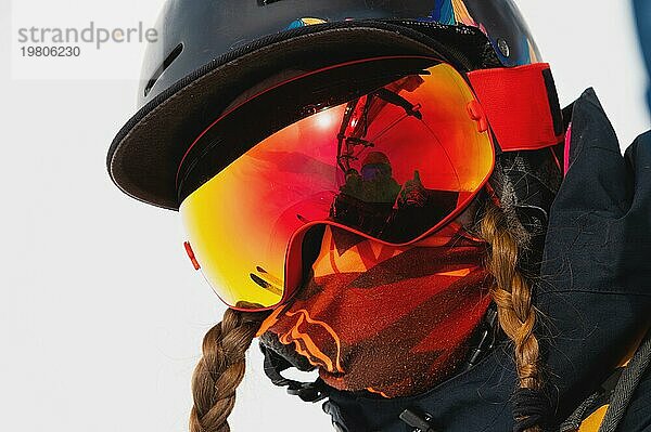 Porträt einer gesunden jungen Frau mit Sportmaske und Helm im Winterurlaub in den verschneiten Bergen. Das Mädchen fährt mit einem Lift und schaut in die Kamera