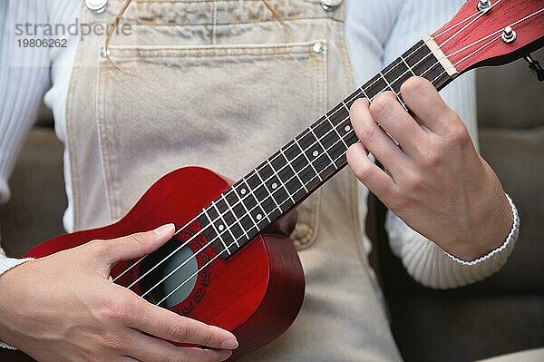 Junge Frau spielt rote Ukulele zu Hause  sitzt auf dem Boden  als Hipster gekleidet  und lernt Lieder